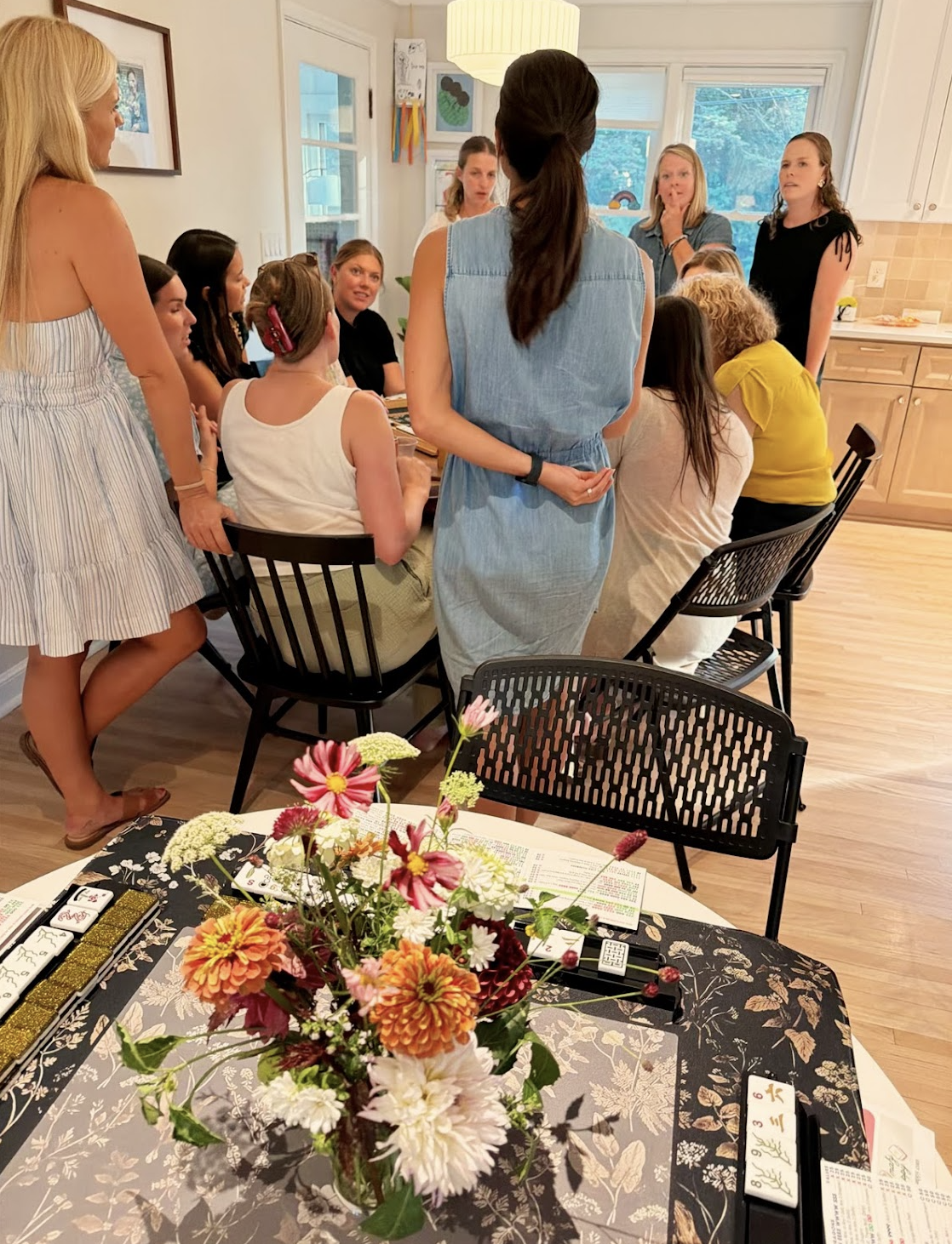 A group gathered around a mahjong lesson table with flowers and tiles