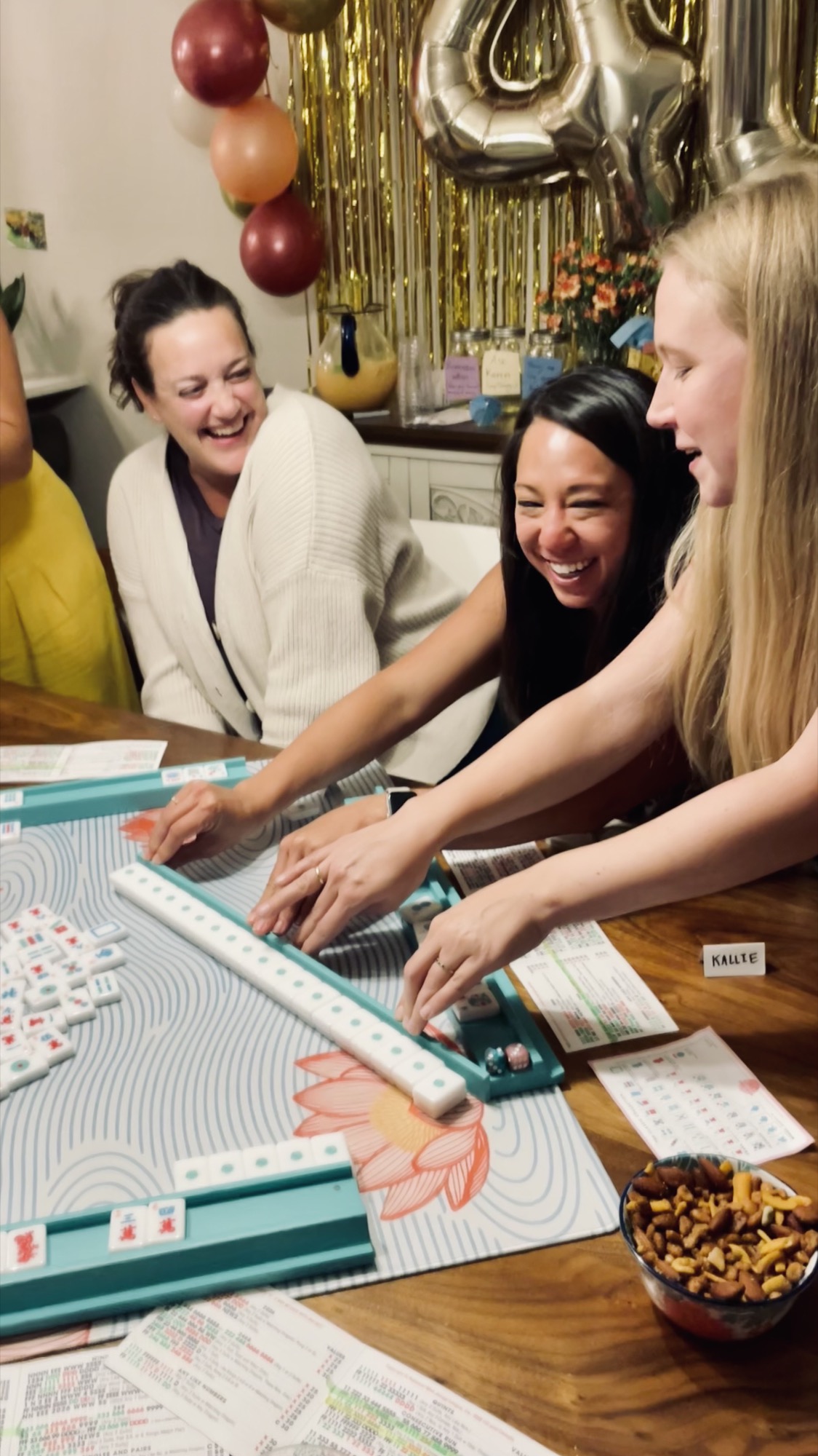 Mahjong players laughing and reaching for tiles together