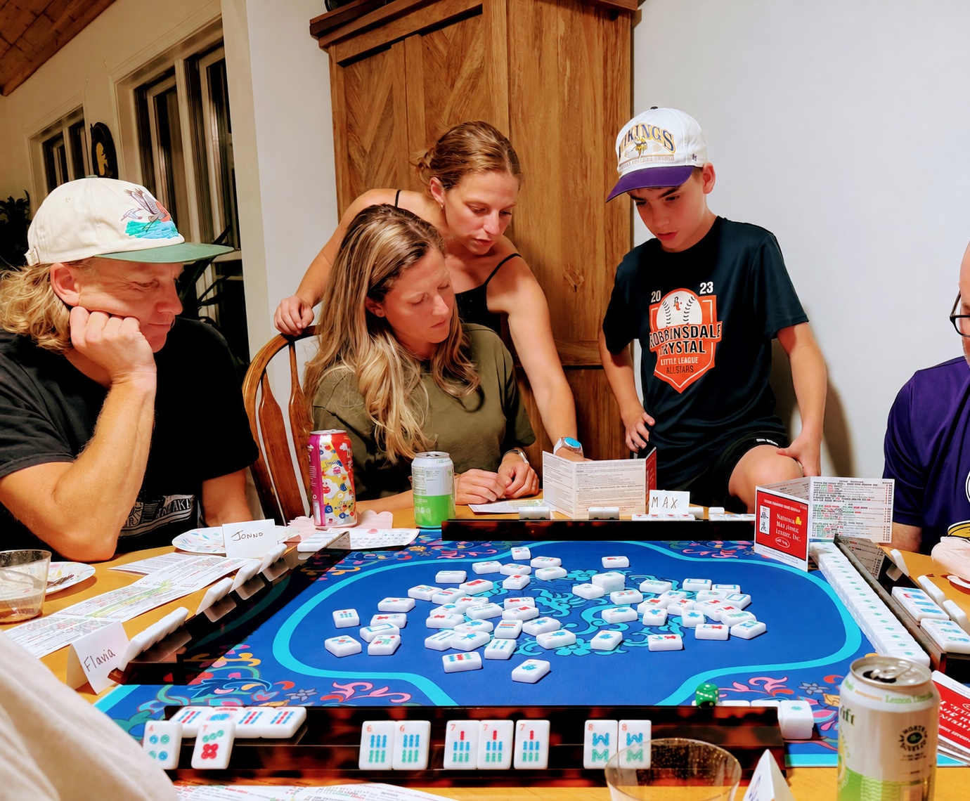An instructor helping a mixed-age group play around a blue mahjong mat