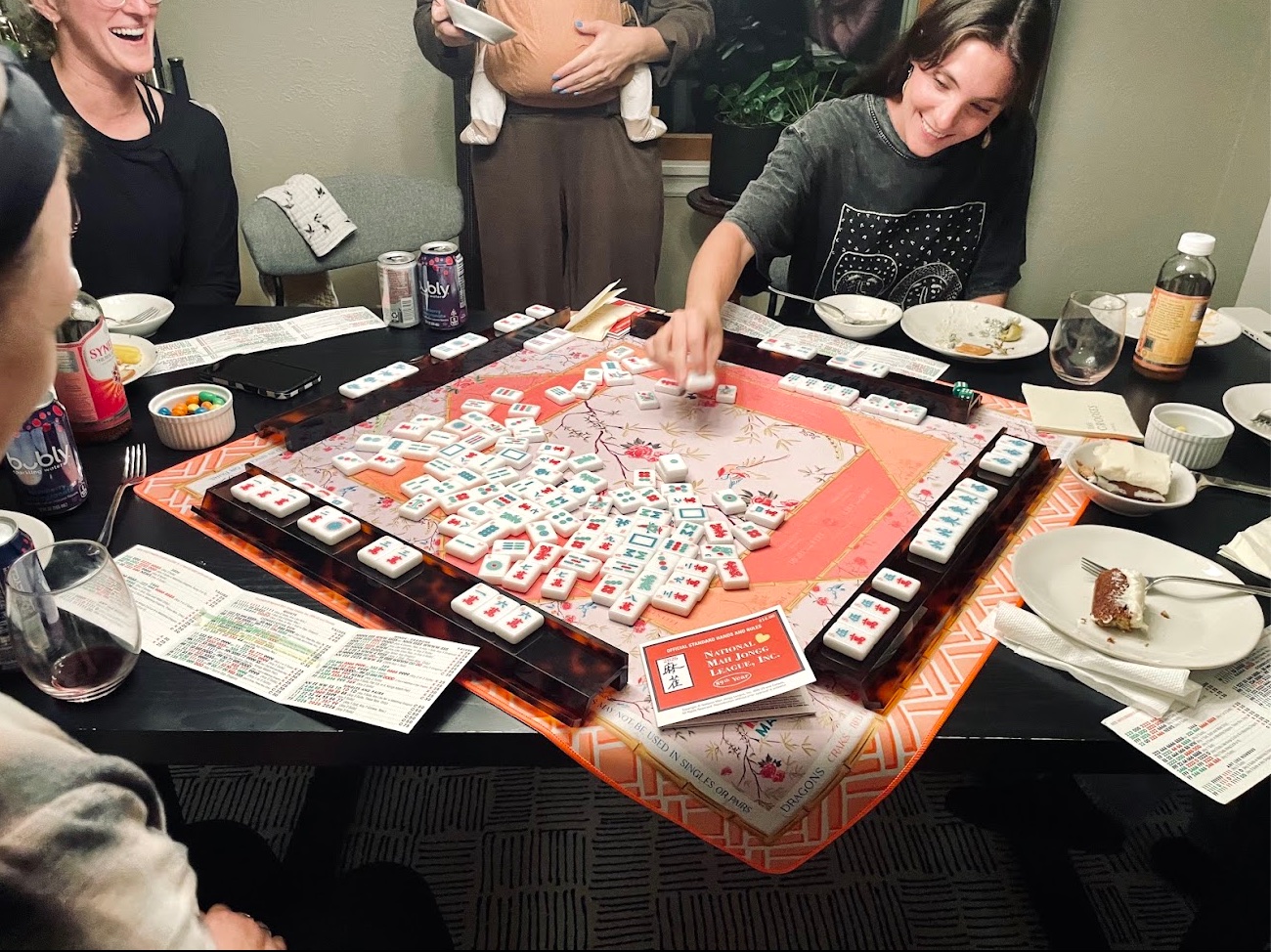 Players laughing and reaching for tiles around a pink mahjong mat